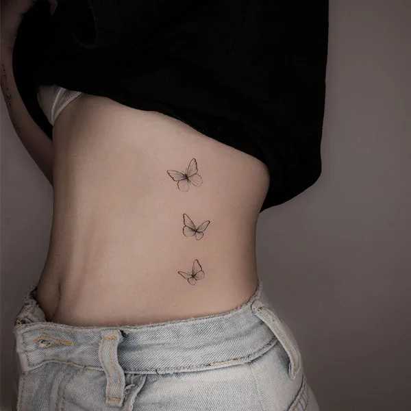 H&igrave;nh xăm ba con bướm nhỏ tr&ecirc;n v&ugrave;ng bụng của một người mặc quần jean v&agrave; &aacute;o tối m&agrave;u.