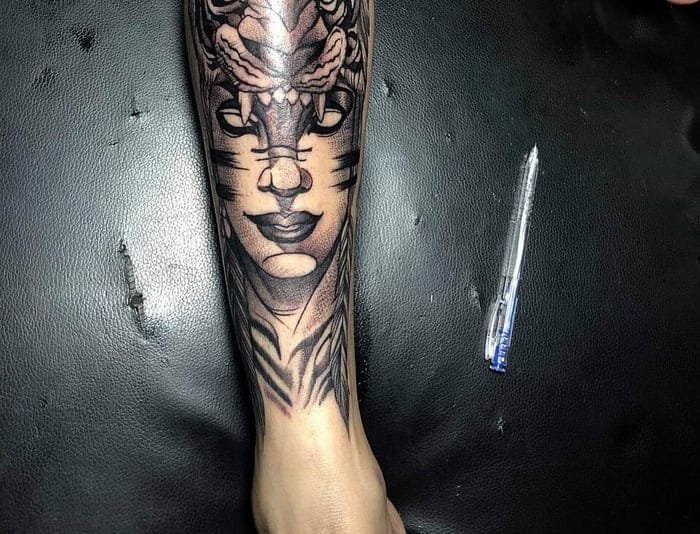 Hình xăm trên cánh tay với hình vẽ mặt nạ và rồng, bên cạnh là một chiếc bút bi trên nền đen.