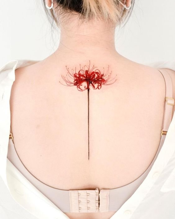 H&igrave;nh xăm hoa m&agrave;u đỏ tr&ecirc;n lưng người, với c&aacute;nh hoa chi tiết v&agrave; th&acirc;n d&agrave;i, dưới &aacute;nh s&aacute;ng tự nhi&ecirc;n.