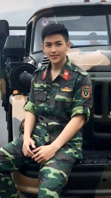 Người mặc quân phục ngồi trên xe quân sự, nền trời mây xám.