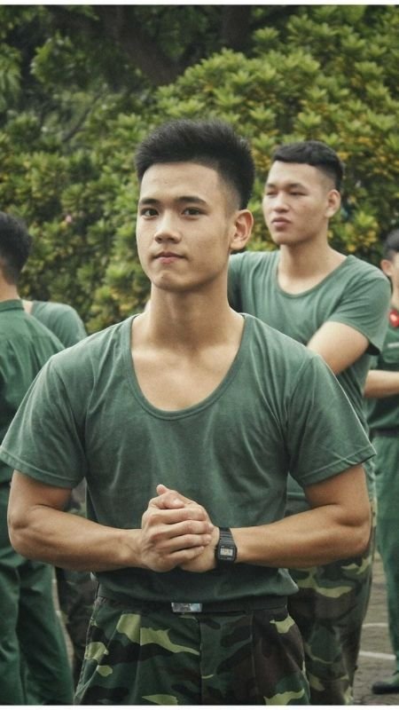 Một nhóm người mặc đồng phục quân đội màu xanh lá cây đứng ngoài trời, người phía trước đang đan tay.