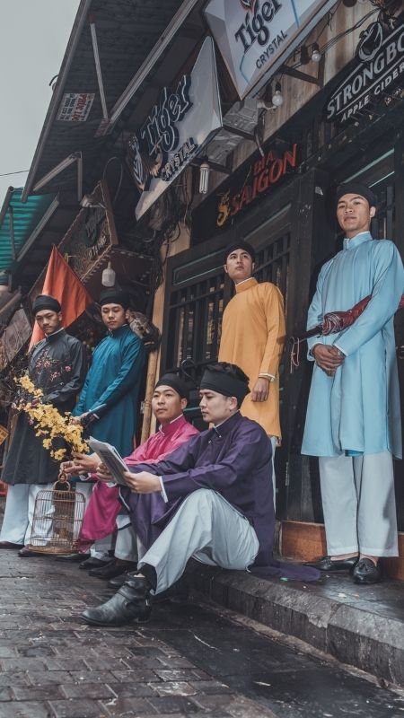 Nhóm người mặc áo dài truyền thống đứng và ngồi trước cửa hàng trên phố cổ, bầu không khí cổ điển.