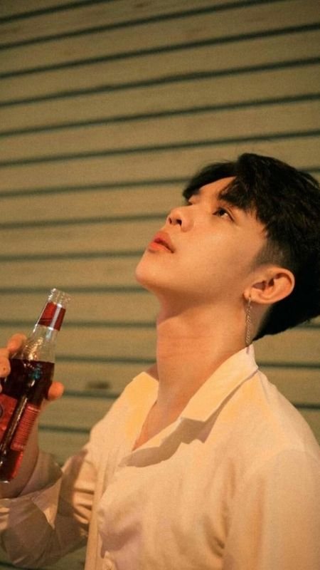 Người đang cầm chai nước, nhìn lên trên, mặc áo sơ mi trắng, đứng trước nền vân ngang.