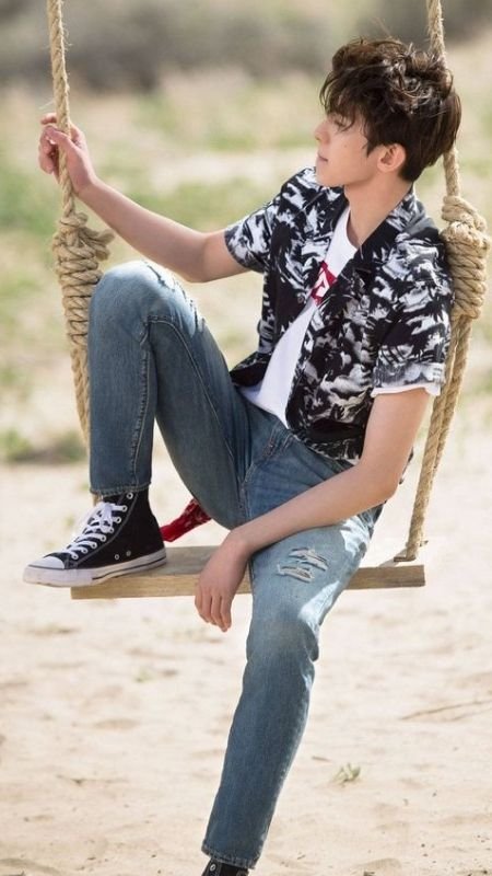 Người trẻ ngồi trên xích đu gỗ ngoài trời, mặc áo sơ mi họa tiết và quần jeans, nhìn xa xăm.