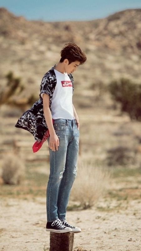 Người mặc áo thun trắng và quần jeans đứng trên cọc gỗ, phông nền là cảnh quan sa mạc.
