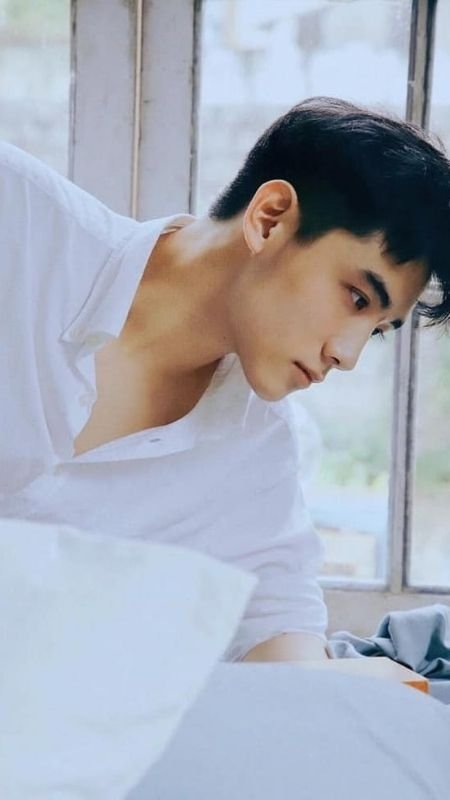 Người đàn ông mặc áo sơ mi trắng, đang ngồi gần cửa sổ với ánh sáng tự nhiên chiếu vào.