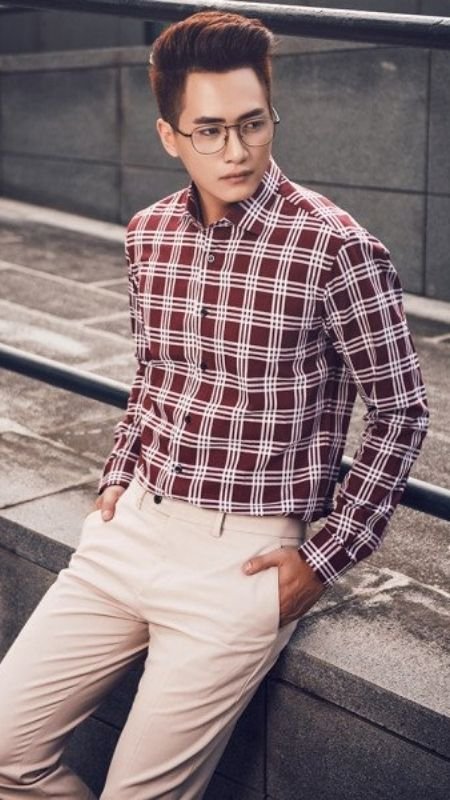 Người đàn ông mặc áo sơ mi caro, quần sáng màu, đứng tựa vào lan can ngoài trời.