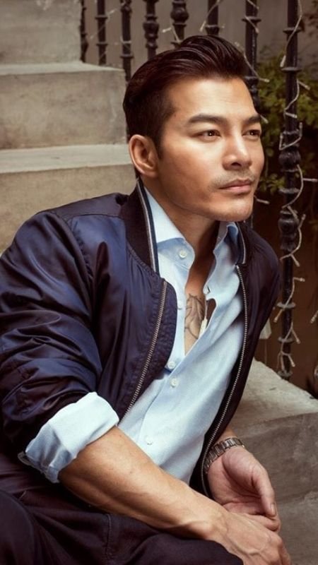 Người đàn ông ngồi trên bậc thang, mặc áo sơ mi trắng và áo khoác xanh, nhìn xa xăm.