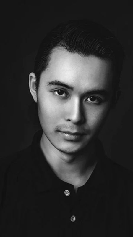 Chân dung một người đàn ông trẻ tuổi trong ảnh đen trắng, mặc áo sơ mi tối màu, nhìn thẳng vào máy ảnh.