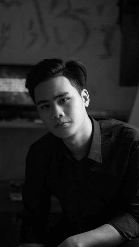 Chân dung đen trắng của một người đang ngồi, nhìn về phía máy ảnh, phông nền mờ.