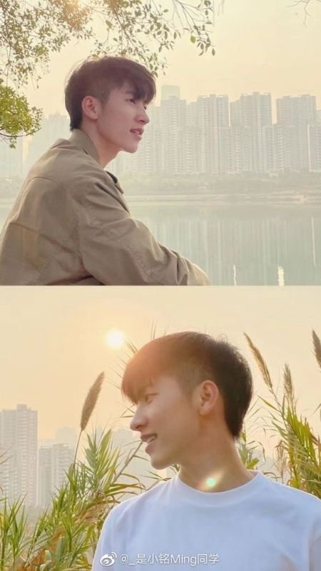 Hai người đứng ngoài trời, một người ngồi cạnh hồ, người kia đứng gần cỏ lau, nền là khung cảnh thành phố.