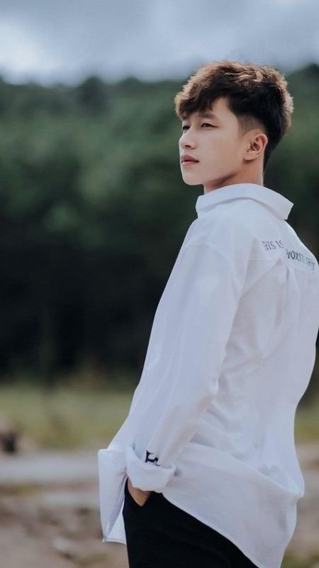 Người mặc áo sơ mi trắng đứng trong khung cảnh thiên nhiên xanh mát, nhìn xa xăm về phía chân trời.