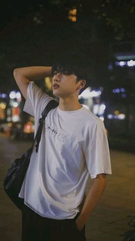 Người mặc áo phông trắng và túi đeo vai đứng dưới ánh đèn đường vào buổi tối.